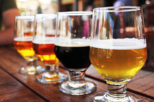 closeup photo of four glasses of beer of varying colors aligned atop a dark wooden bar