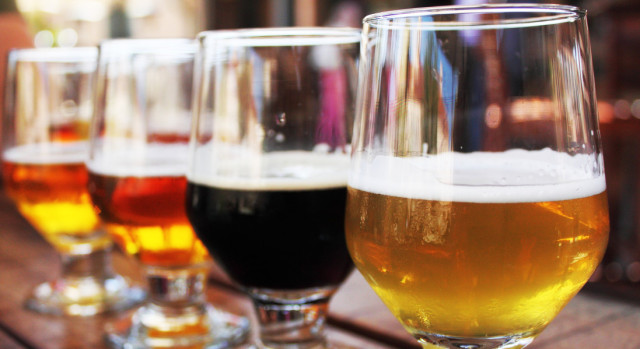 closeup photo of four glasses of beer of varying colors aligned atop a dark wooden bar